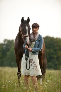 Woman standing beside a Hanoverian horse in a meadow