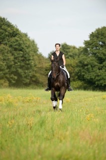 Woman riding a galloping Holsteiner horse across a meadow