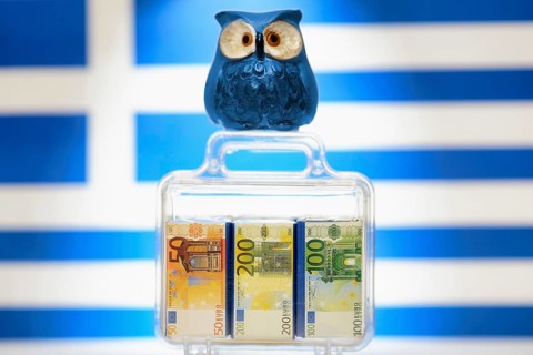 Owl on a suitcase full of money in front of a Greek flag