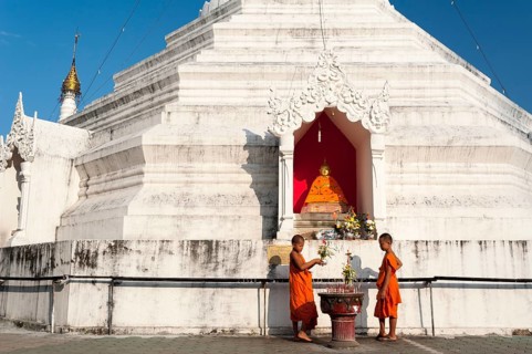 Young Buddhist monks with offerings in front of a Pagoda or Chedi
