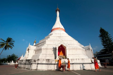 Young Buddhist monks with offerings in front of a Pagoda or Chedi