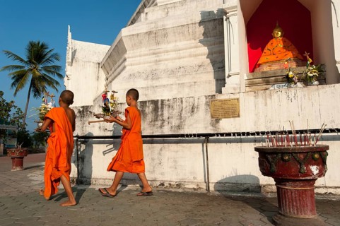 Young Buddhist monks with offerings in front of a Pagoda or Chedi