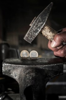 Greek euro coins under pressure in a vice and threatened by a hammer