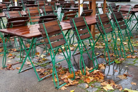 Empty tables and chairs of an outdoor restaurant in the rain with autumn leaves in the historic city centre of Cologne