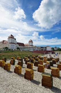 Roofed wicker beach chairs on the beach in front of the Kurhaus spa building