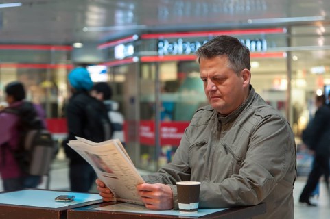 Man standing in a shopping mall reading a newspaper