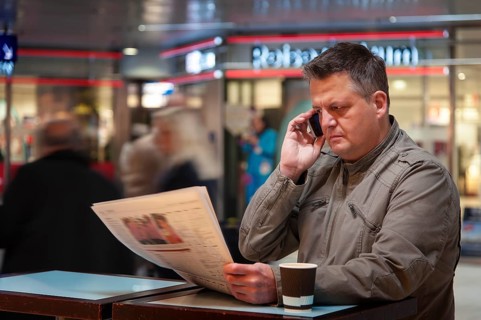 Man on a mobile phone reading a newspaper