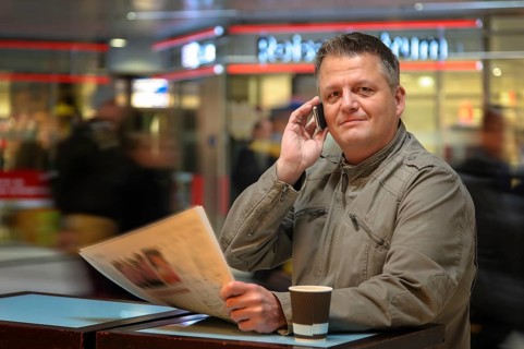 Man with a newspaper and a mobile phone in a shopping mall
