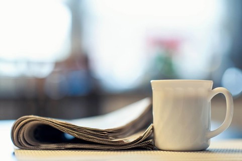 A cup of coffee and a newspaper lying on a kitchen table