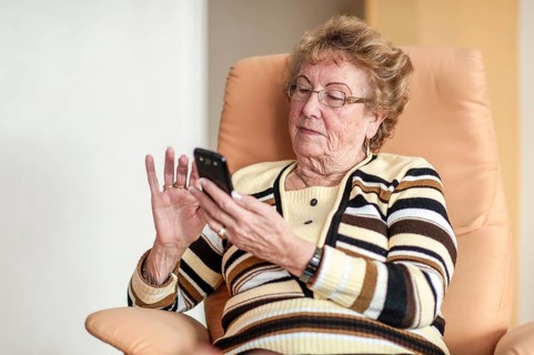 Elderly woman sitting in an armchair and using a smartphone
