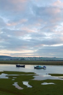 Two small boats rising with incoming tide on tidal stretch of river at dawn