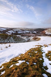 View of lingering snow on moorland hills and fields in late afternoon sunshine