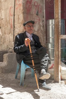 Old man with a walking stick seated on a plastic chair