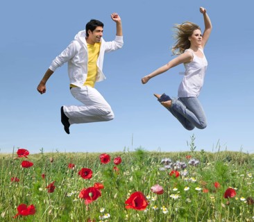 Young couple jumping over a flower meadow in early summer