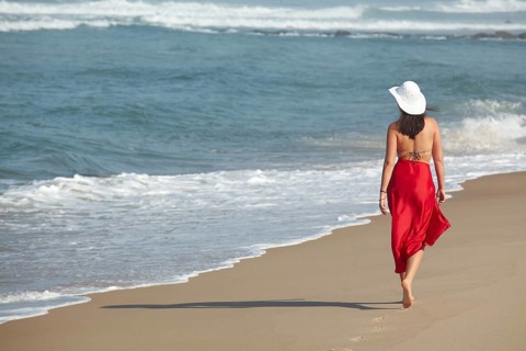 Rear view of a young woman wearing a bikini and a red sarong walking along a beach in summer