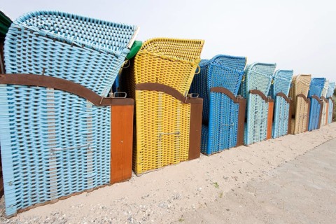 Perspective image of a row of blue and yellow roofed wicker beach chairs