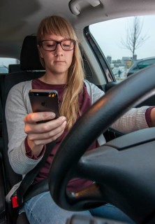 Young woman driving a car while texting on her cell phone