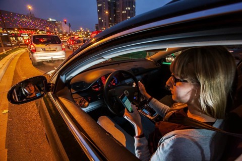 Young woman driving a car in the city centre in the evening while texting on her cell phone