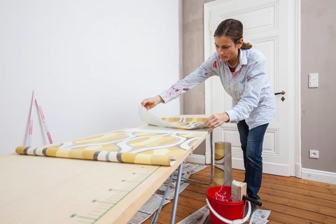 Young woman preparing wallpaper for wallpapering the walls