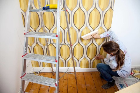 Young woman wallpapering a wall
