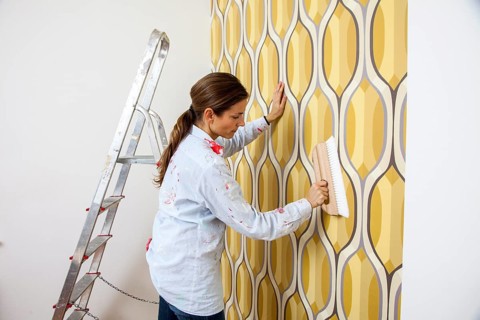 Young woman wallpapering a wall