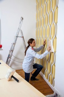 Young woman wallpapering a wall