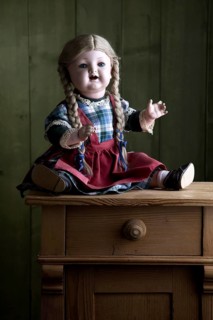 Antique doll sitting on a small chest of drawers