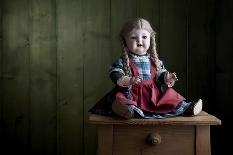 Antique doll sitting on a small chest of drawers