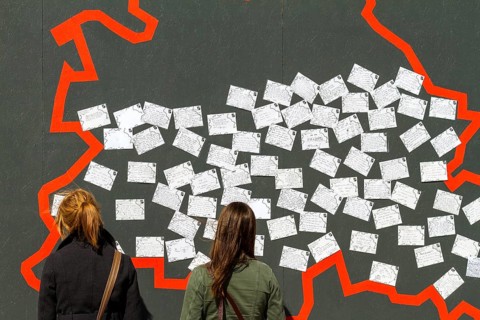 Two young female tourists standing in front of a wall with postcards