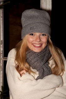 Smiling young woman wearing a cap and a scarf standing in front of a hiking hut