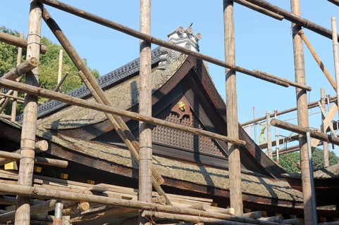 Shrine building is surrounded by scaffolding consisting of long logs