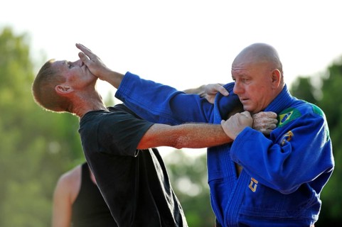 A martial arts instructor is demonstrating a defensive move on a student in a park