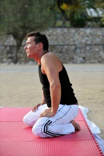 A martial arts student is kneeling on an exercise mat in a park