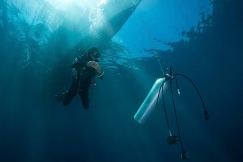 Diver with spare air tank during a decompression stop under a boat