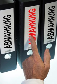 Hand pointing to a ring binder labelled "ABMAHNUNG"