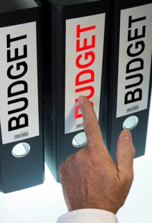 Hand pointing to a ring binder labelled 'BUDGET'
