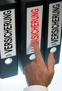 Hand pointing to a ring binder labelled 'VERSICHERUNG'