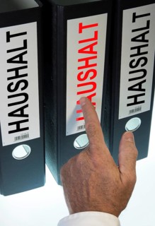 Hand pointing to a ring binder labelled "HAUSHALT"