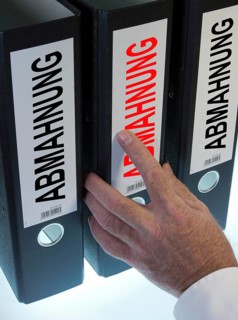 Hand reaching for a ring binder labelled 'ABMAHNUNG'