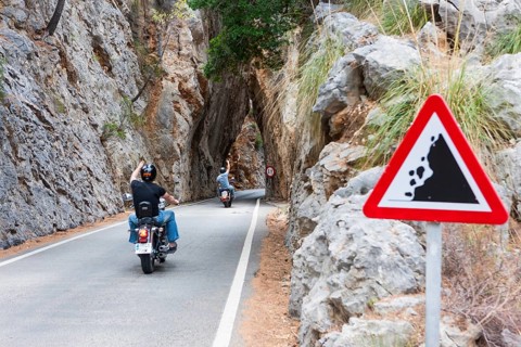 Motorcyclists drive through a narrow tunnel along the winding mountain road to Sa Calobra