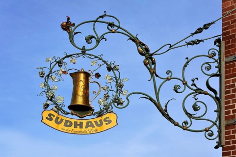 Hanging sign from the restaurant Sudhaus against a blue sky
