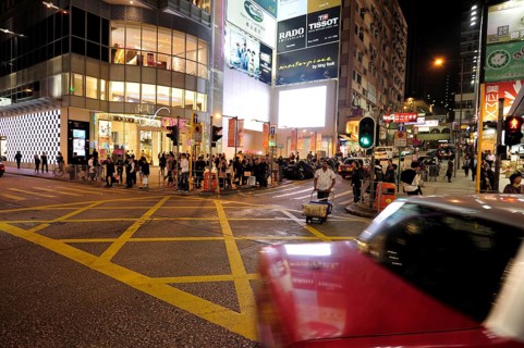 A red taxi driving on a street in Tsim Sha Tsui in the evening