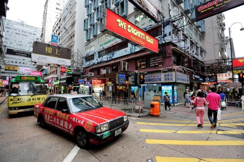 A red taxi waiting at a zebra crossing on a street in the Tsim Sha Tsui district