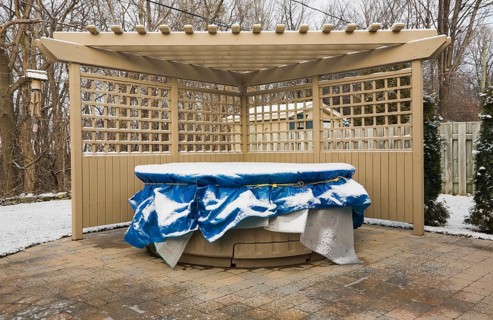 Wooden pergola and a spa in a residential backyard covered up for the winter season