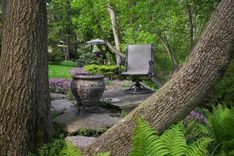 View through two tree trunks of a planter and a chair on a raised platform in a landscaped backyard garden in spring