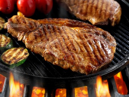 Sirloin beef steaks and tomatoes being pan fried on a BBQ