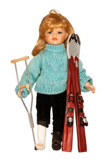 Doll with ski clothing and skis with her foot in plaster and holding a crutch following a ski accident