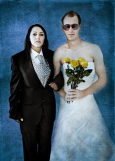 Bride wearing a suit and a groom wearing a wedding dress with sunglasses and yellow roses