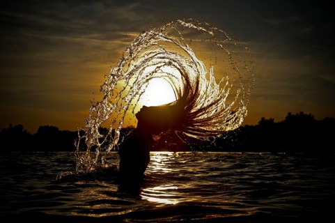 Young woman standing in the sea throwing back her long hair with splashing water