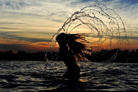 Young woman standing in the sea throwing back her long hair with splashing water